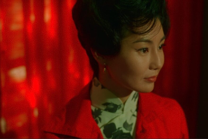 The face of the actor Maggie Cheung Man Yuk, with a beehive hairdo, wearing a red jacket, in a still from the film In the Mood for Love.