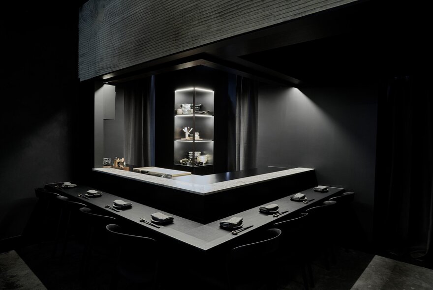 A sophisticated black dining space with low lighting centred around a chef station. 