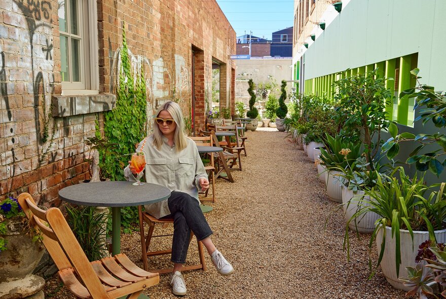 A woman drinking an Aperol spritz in a laneway bar.