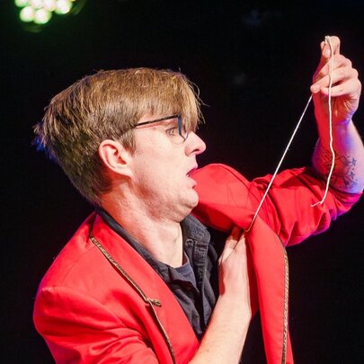 A magician performing on stage and pulling a string from underneath his red jacket. 