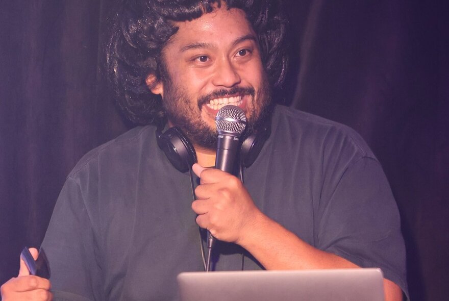 Comedian David Correos performing stand up on a stage, holding a microphone. 