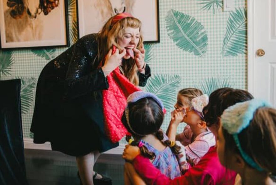 Performer Magical Katrina poking out her tongue and making a funny face at a group of children seated on the floor in front of her.