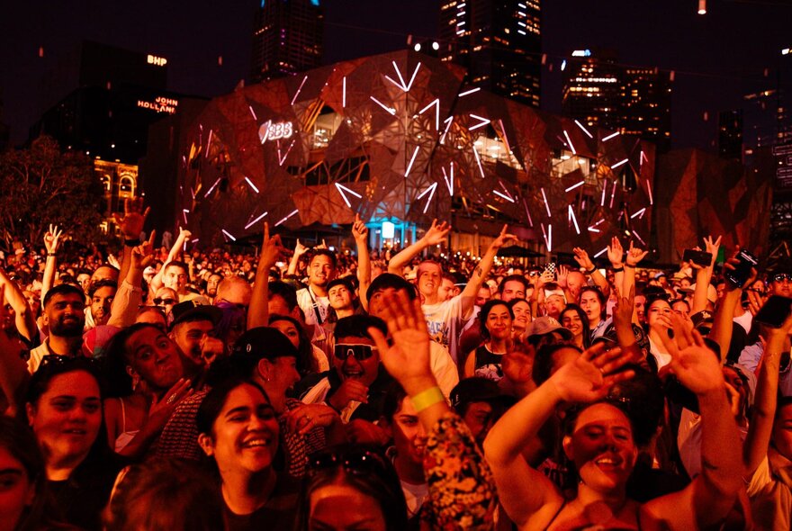 A large crowd of people listening to live music and enjoying themselves at the main plaza at Fed Square. 