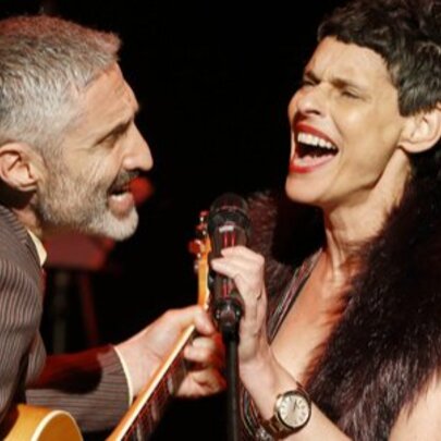 Musicians Deborah Conway and Willy Zygier singing vigorously into one microphone. 