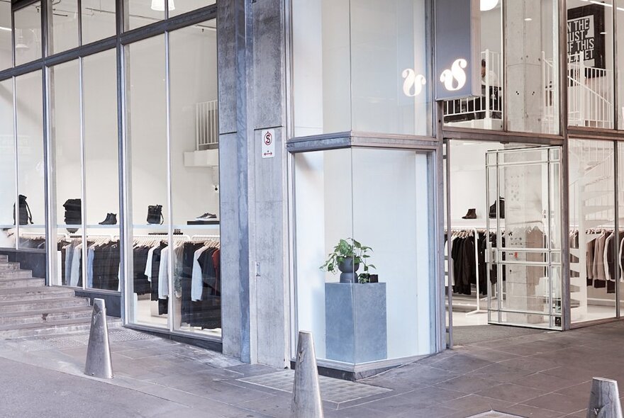 A glass, concrete and metal building with clothing displayed inside.
