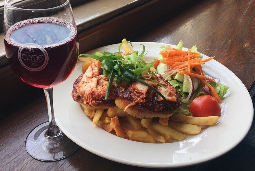 A glass of wine next to a plate of parmigiana, chips and salad.