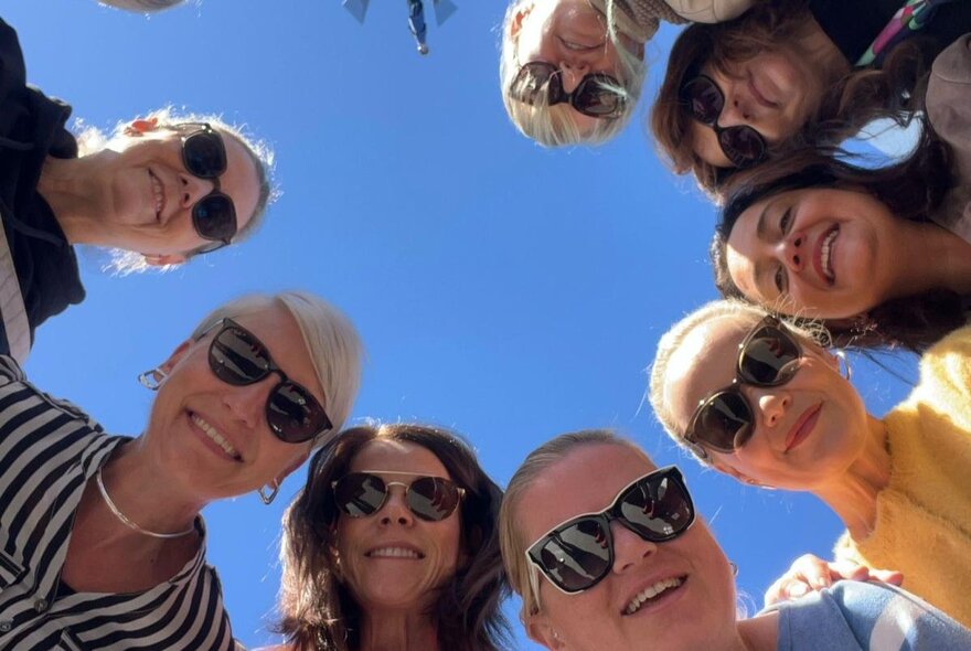 A group of women in a huddled circle looking downwards at the camera, smiling. 