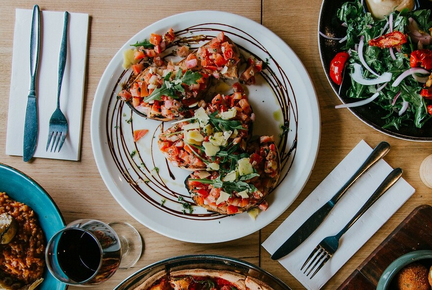 Table setting with wine, cutlery, seafood dish, pizza and salad.