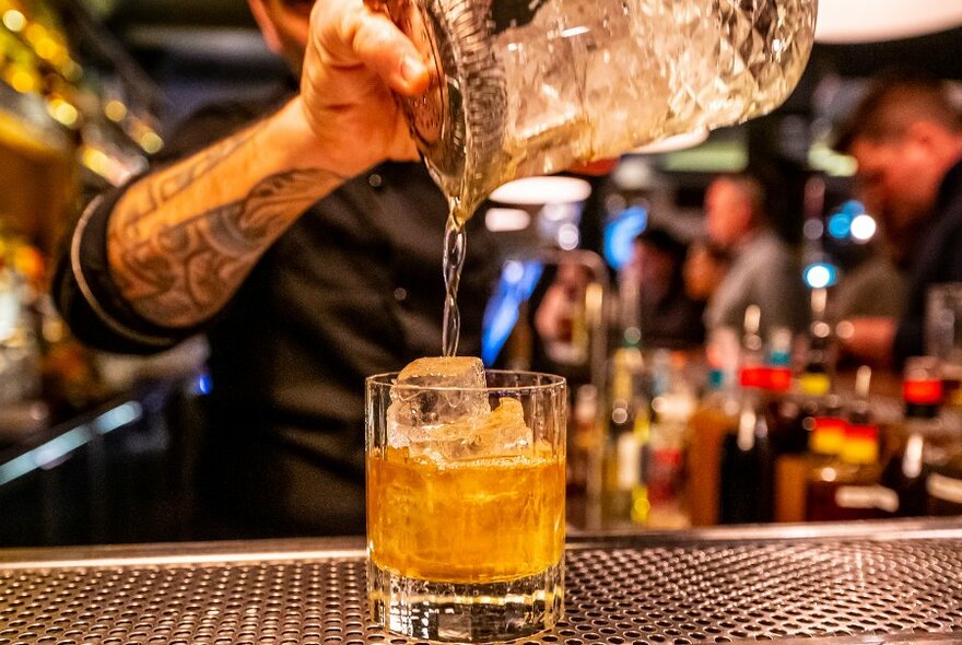 A bartender pouring a cocktail into a glass