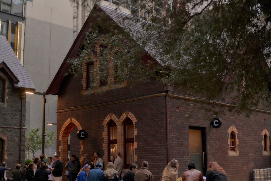 People seated outside the brick Caretaker's Cottage bar on a winter's day as light is fading.