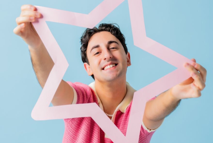 A man smiling and holding up a pink border of a star.