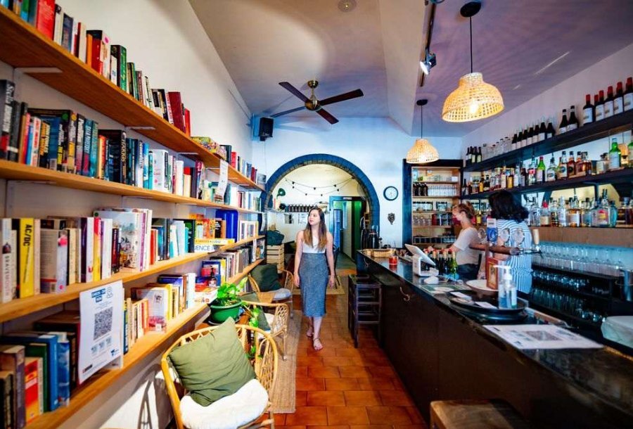 A woman walking through a wine bar with a bookshelf.
