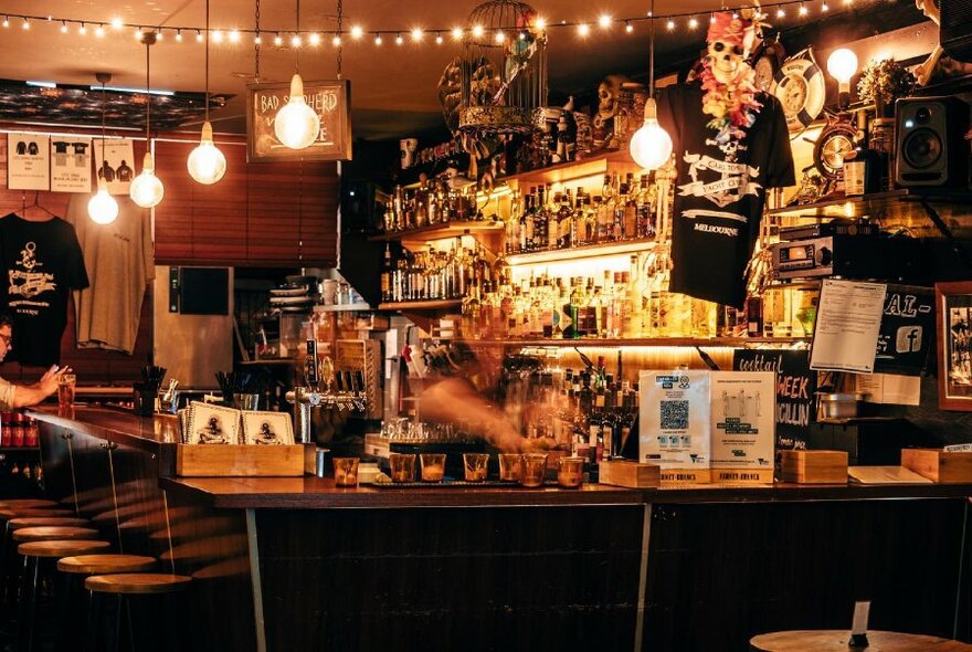 View onto a wooden bar, with bottles behind the counter, bar stools, hanging lights and decor on the walls.