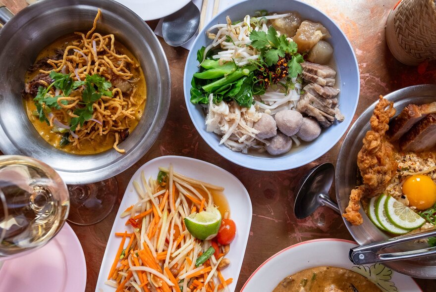 A table of Thai food with noodles, papaya salad and more