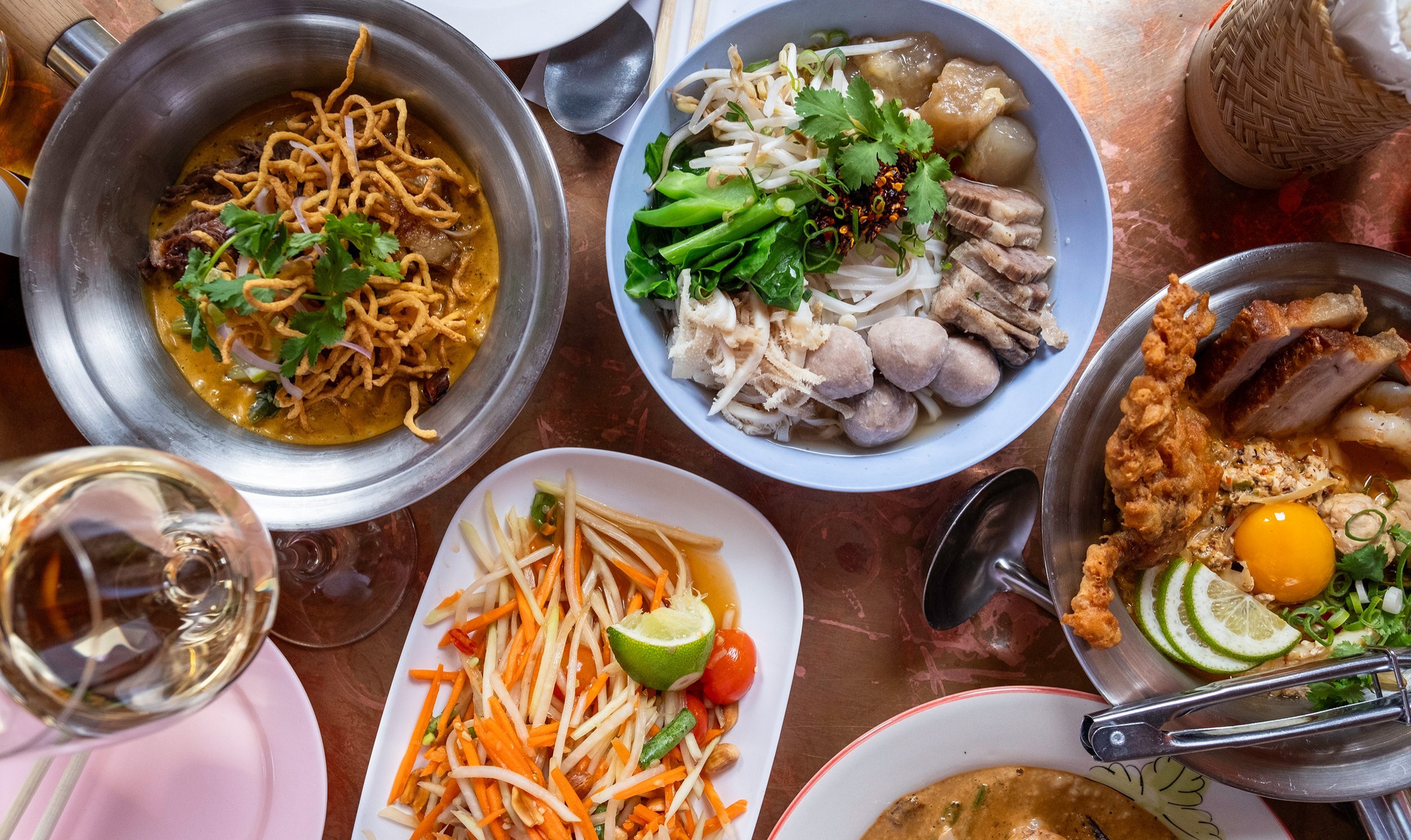 A table of Thai food with noodles, papaya salad and more
