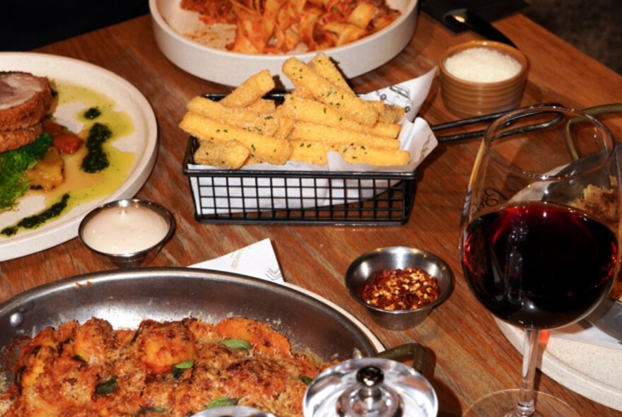 Plates of food and a glass of red wine on a dining table.