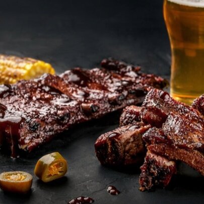 Juicy barbecue ribs next to a pint of beer on a black surface.