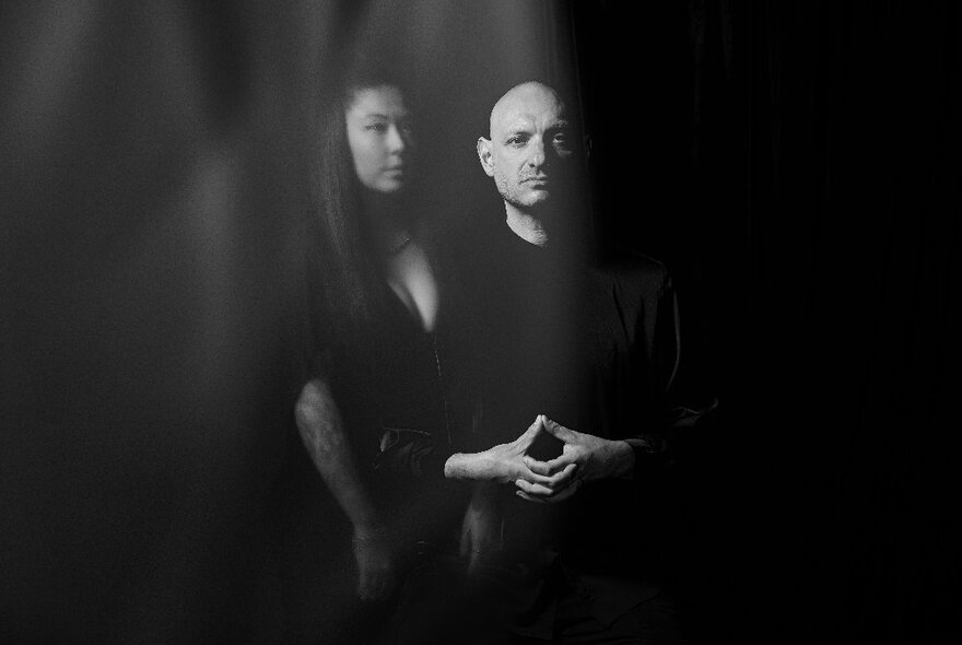 Music duo photographed in black with only faces and hands visible.