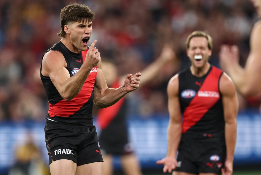 Several Essendon AFL players cheering and looking excited with pumped arms and fists, after scoring during a football match
