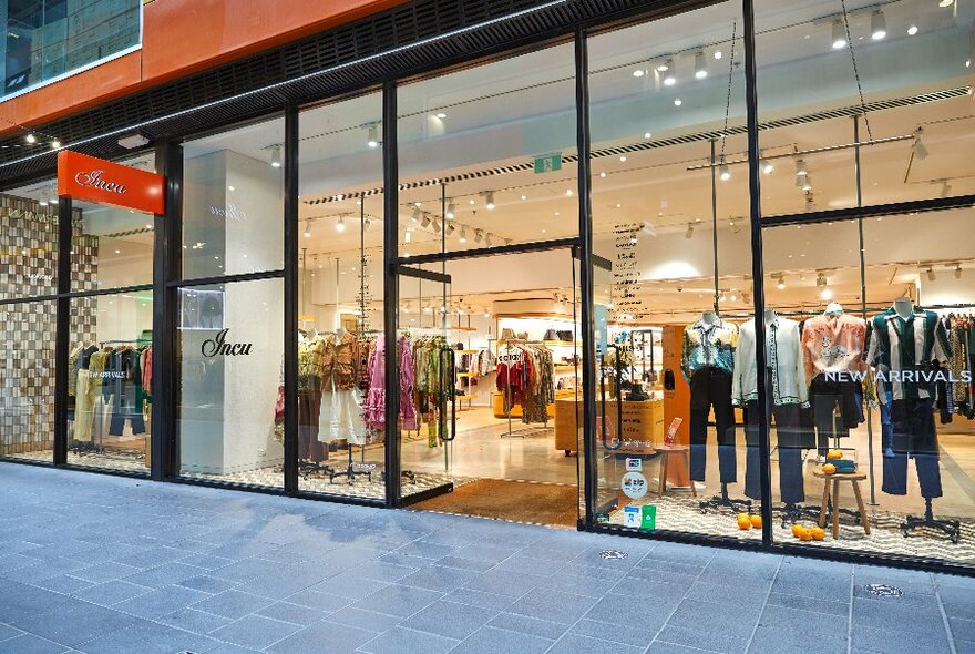 A large fashion boutique with clothing in the windows and bright orange signage.