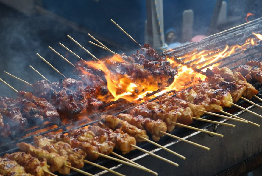 Skewers of meat cooking over an open flame on a BBQ.