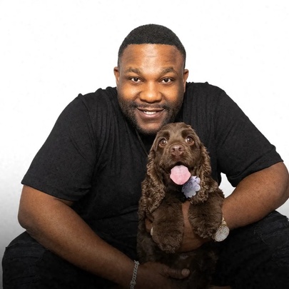 Comedian Nate Jackson poses with a brown spaniel with its tongue out. 