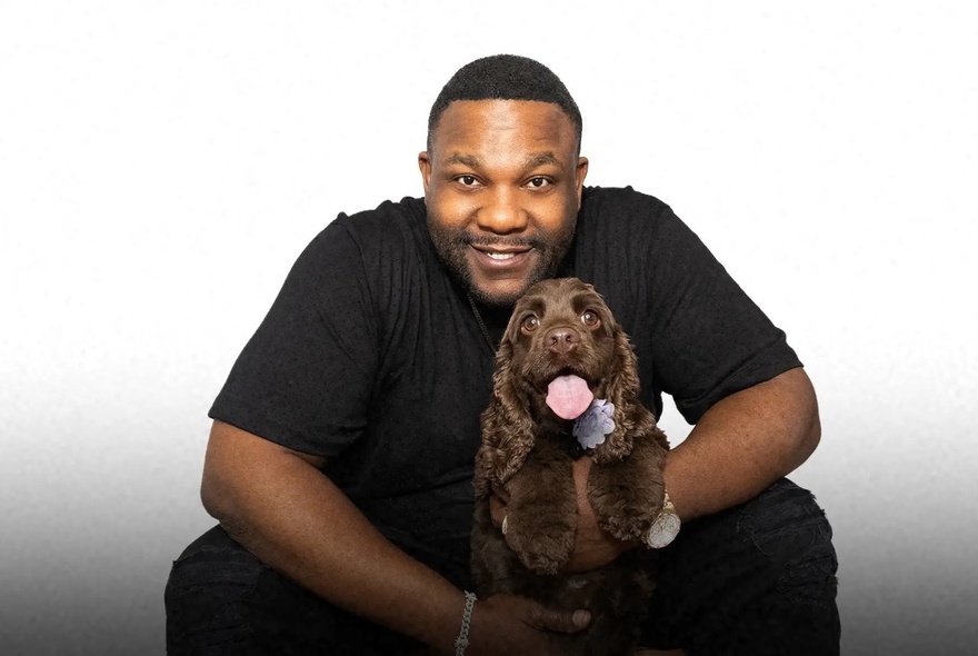 Comedian Nate Jackson poses with a brown spaniel with its tongue out. 