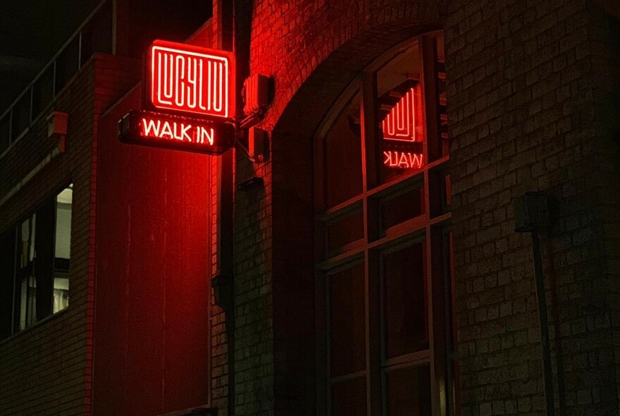 Illuminated red Lucy Liu neon sign on the street at night.