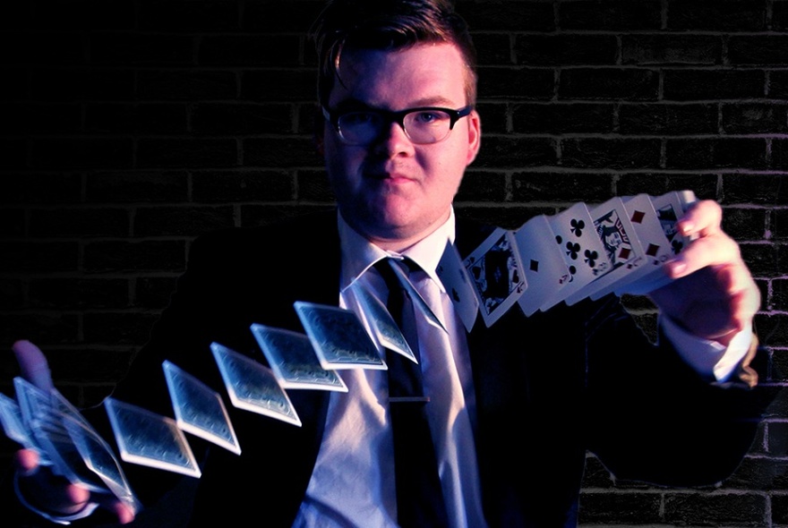 Magician moving a deck of cards between his two outstretched hands while gazing at the viewer.