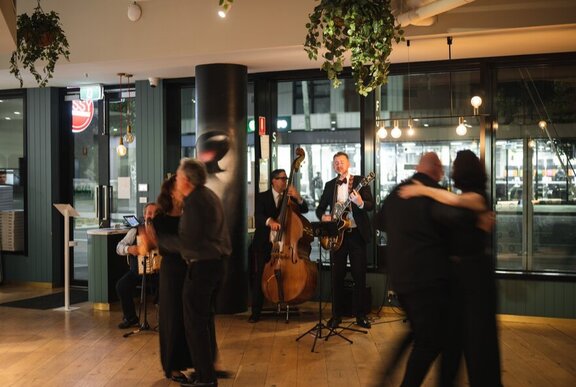 Couples walzing to a live band with double-bass player in an indoor setting.