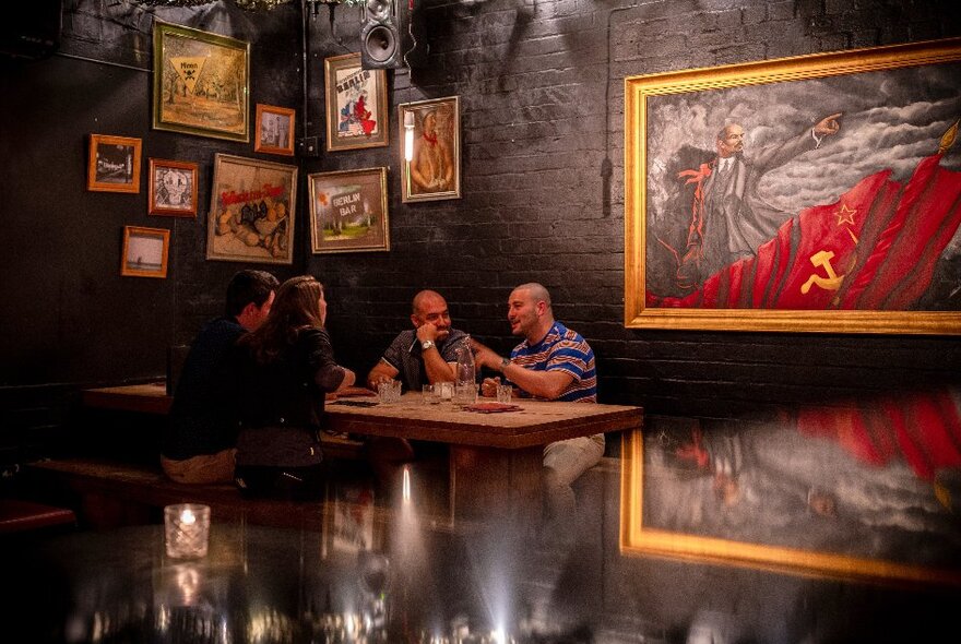 People seated at a table in a dark bar with walls lined with paintings.