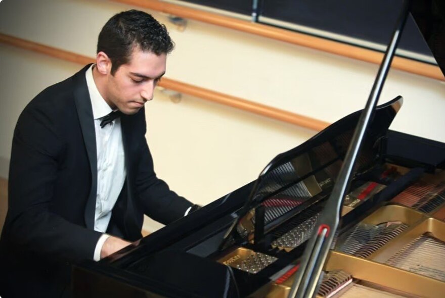 A pianist playing a grand piano, wearing a black tuxedo.
