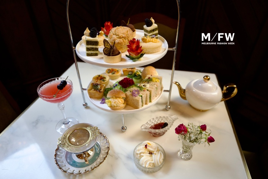 Table set with a tiered sandwich and cake stand, cocktail and teapot.