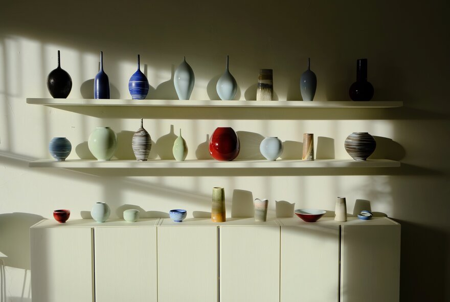 The retail space inside a studio, with ceramics and other objects arranged on shelves against a white wall.