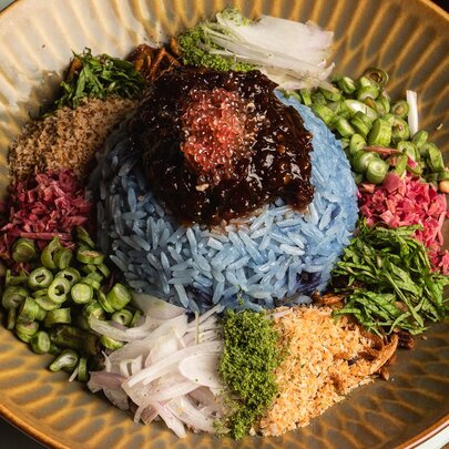 Blue rice with a selection of vegetables and garnishes in a brown dish.