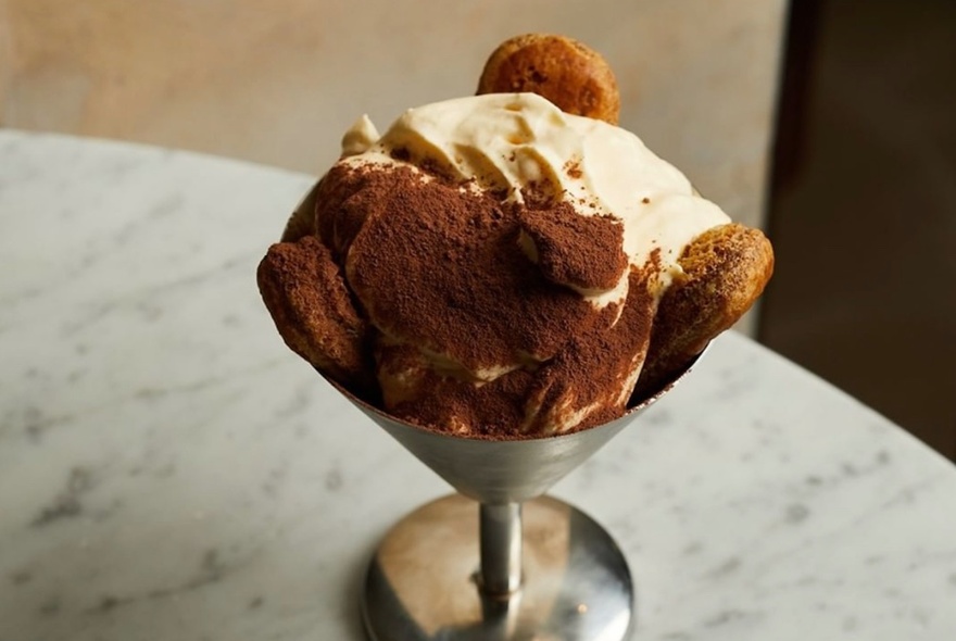 A delicious-looking creamy Italian dessert with biscotti and powdered coffee, presented in a silver martini glass.