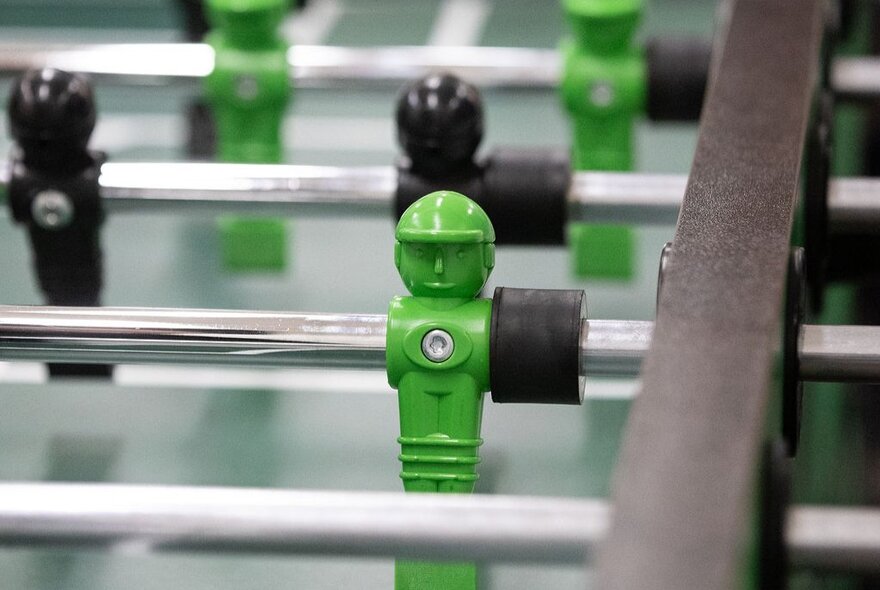 Close up of a foosball table with green and black players.