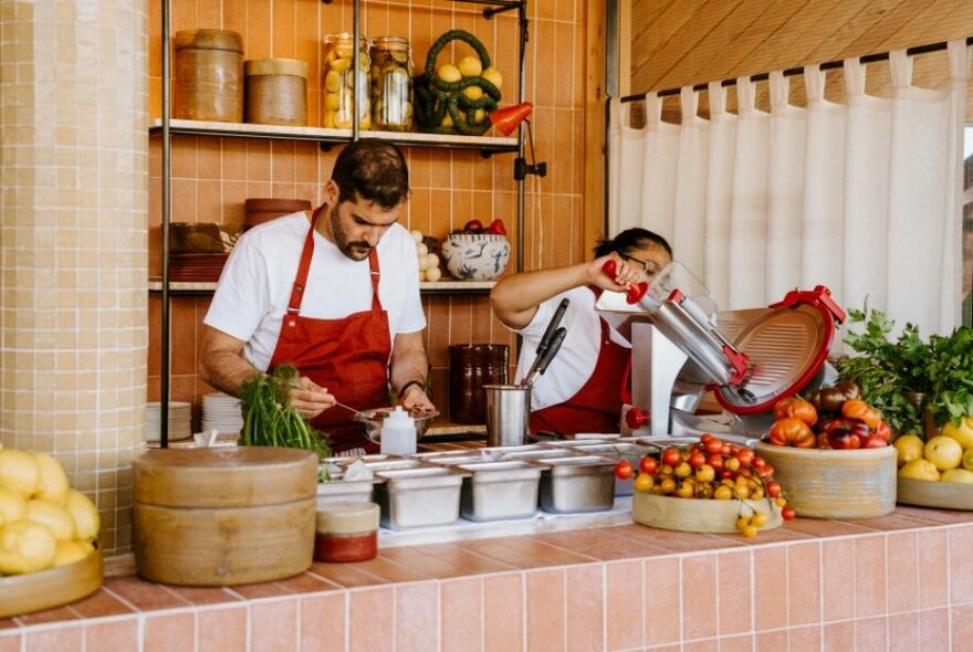 Staff behind a tiled bar preparing food and drinks, with containers of fresh food around them.