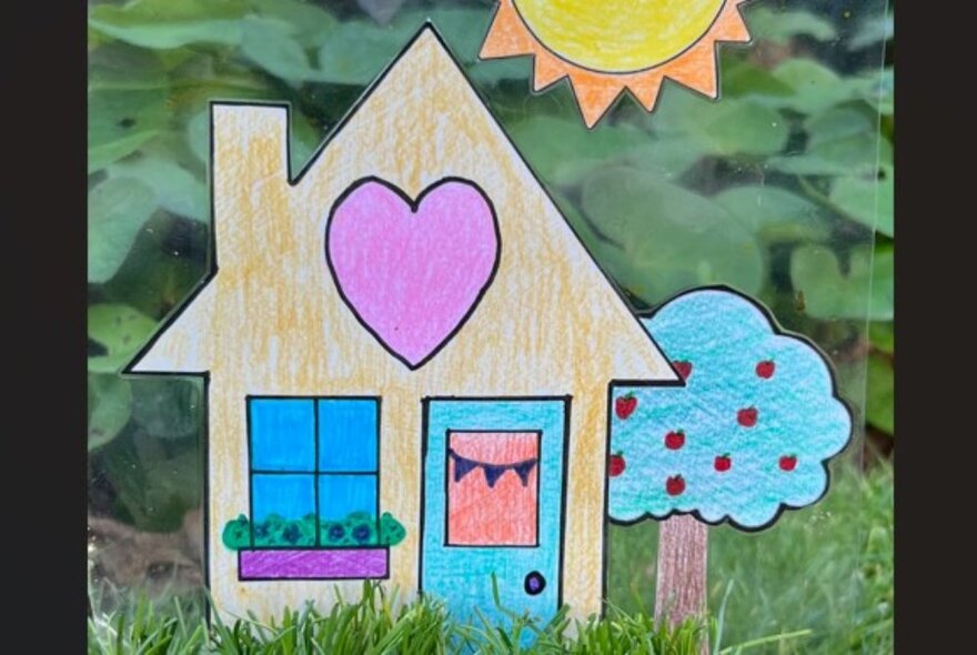 A simple child-like cut out drawing of a house and a tree, with lawn behind it.