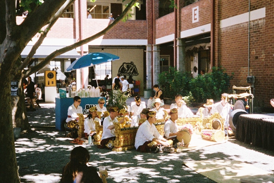 People seated in a shady spot under a tree in a courtyard.