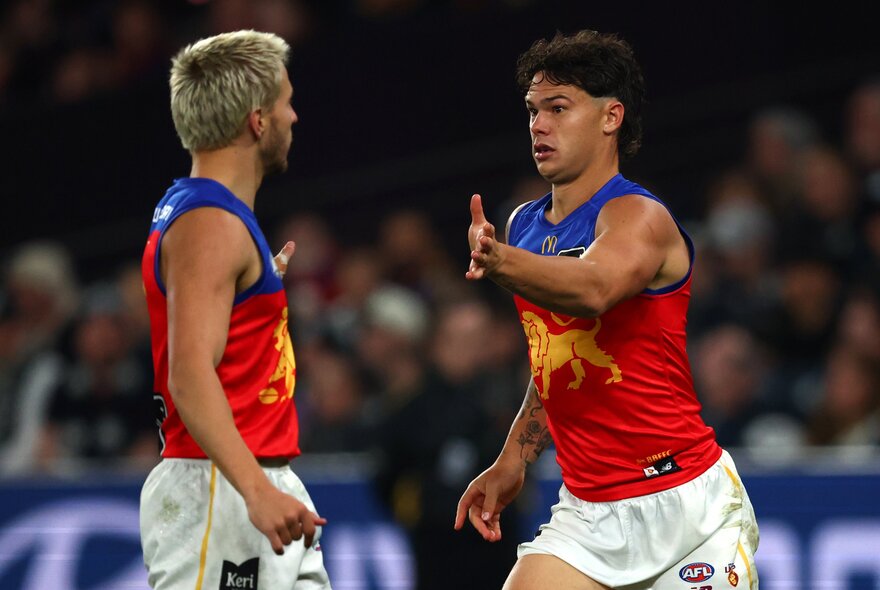 Two Brisbane Lions AFL players about to give each other a high five during a game.