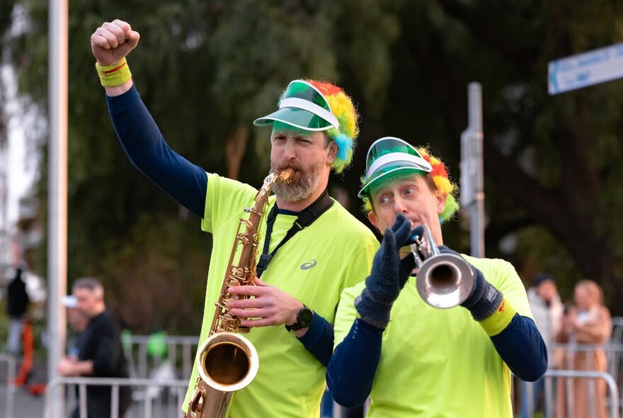 Two people in fluoro t-shirts and coloured clown wigs playing a saxophone and trumpet at the Run Melbourne event.