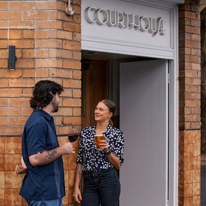 Two people holding beer glasses outside the Courthouse Hotel. 
