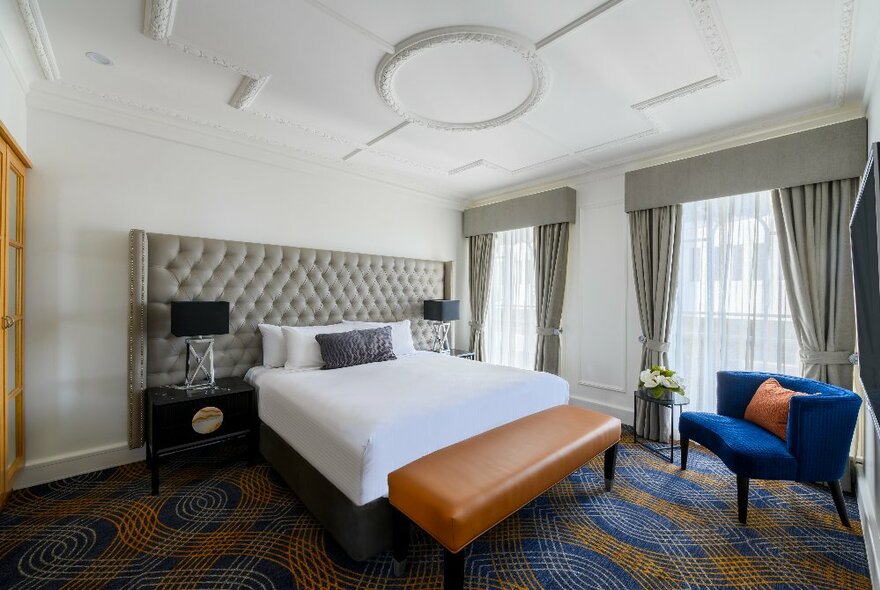 Grand hotel room with ornate art deco ceiling, grey headboard and curtains, and blue details.