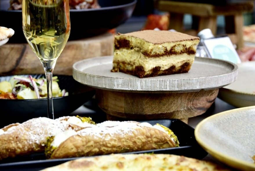 Plate of tiramisu to right of champagne glass, other desserts to front.