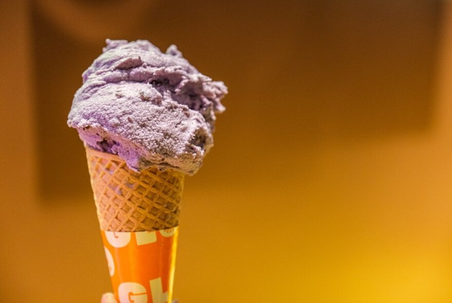 A purple ice cream in a waffle cone with paper wrapping, aligned left. 