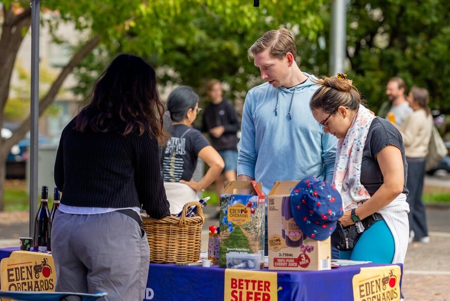 People at an outdoor market in a park looking at a stall. 