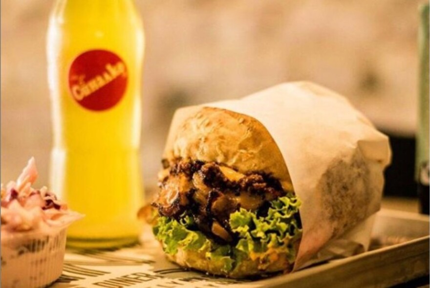 Tray with bottle of lemon soda and a hamburger in paper wrapping.