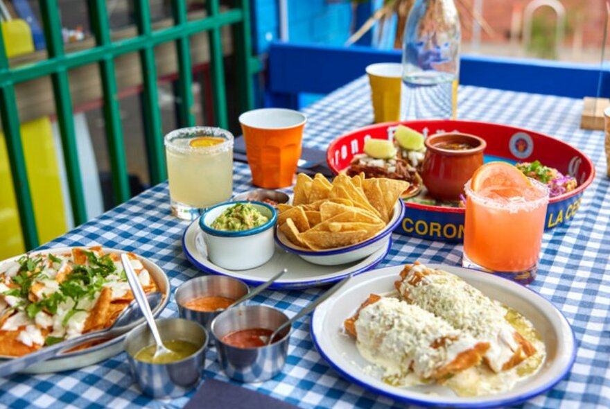 Table with corn chips, guac, nachos, and cocktails.