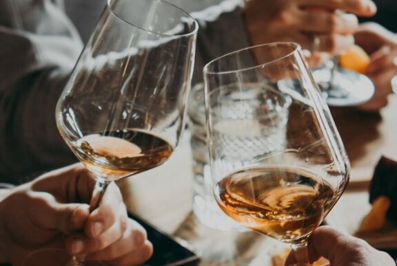 Two hands bringing two wine glasses together so the glasses are almost touching.